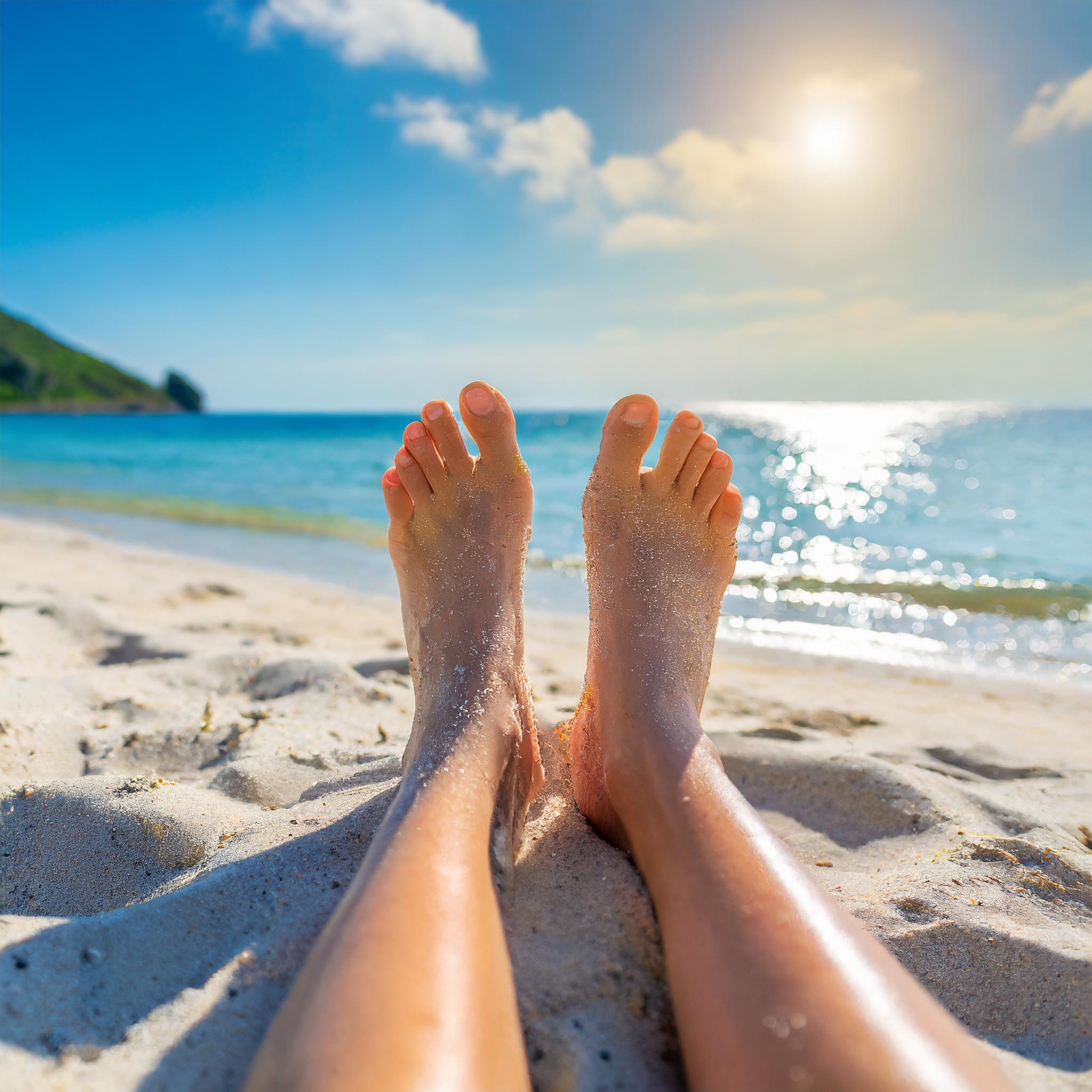 a picture of someone's feet while they are sitting on a beach facing towards the ocean